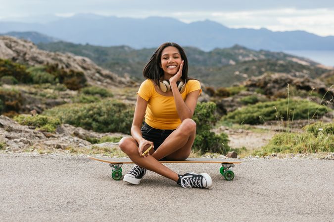 Latina woman sitting on longboard on asphalt road