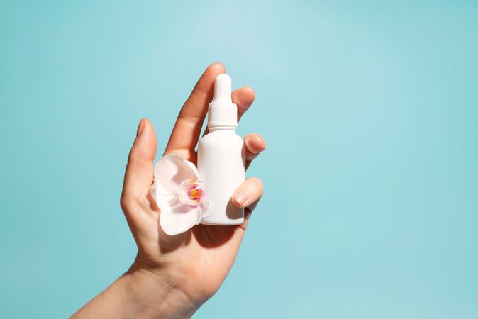 Hand holding cosmetic bottle and flower