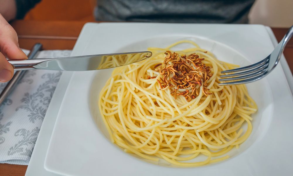Hands of man eating spaghetti with worms