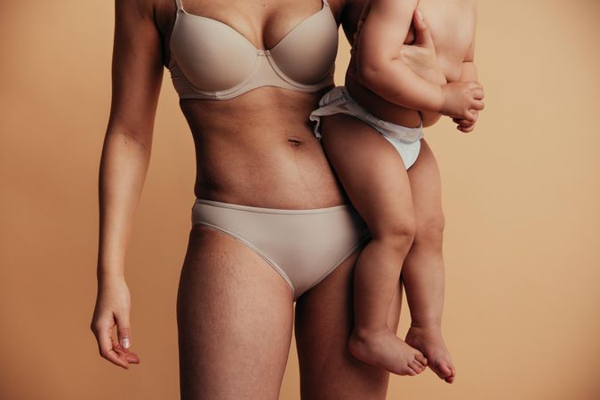 Female wearing tan undergarments and holding baby at her hip
