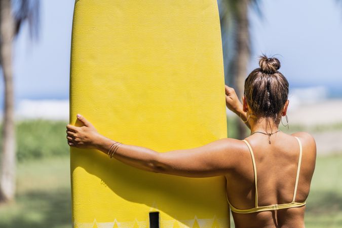 Woman in bikini by bright paddleboard on beach