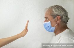 Side view of middle aged man with facemask being stopped by a hand against light background 4ZMOy5