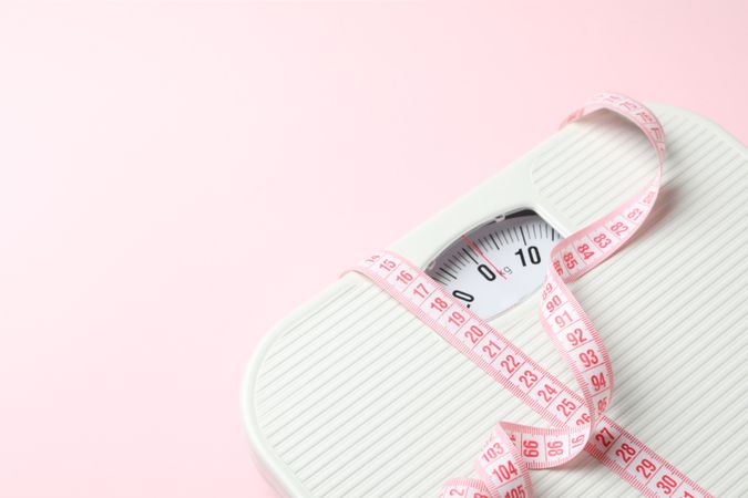 Scales and measuring tape on pink background. Weight loss concept