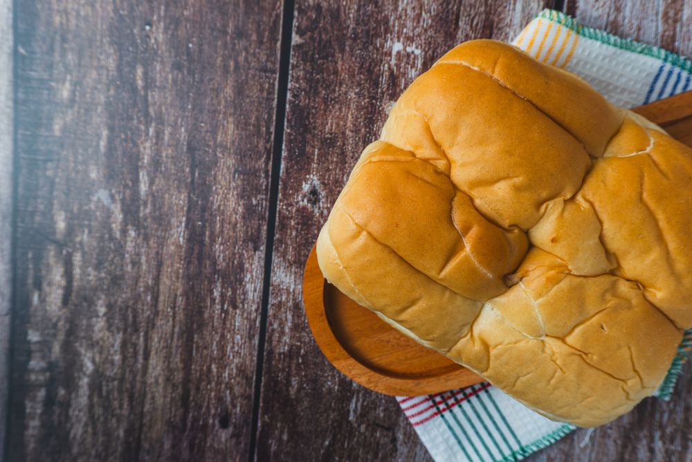A loaf of bread served on a wooden plate placed on a rustic wooden surface
