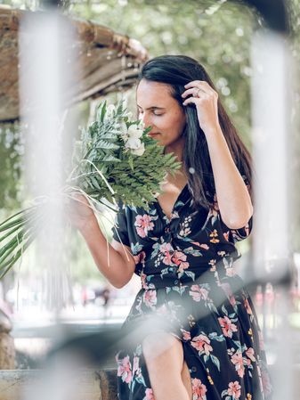 Young female smelling bouquet of flowers resting in park