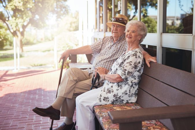 Mature couple having a break while sitting on a bench outside their home