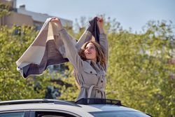 Woman raising arms with scarf and standing in car sunroof