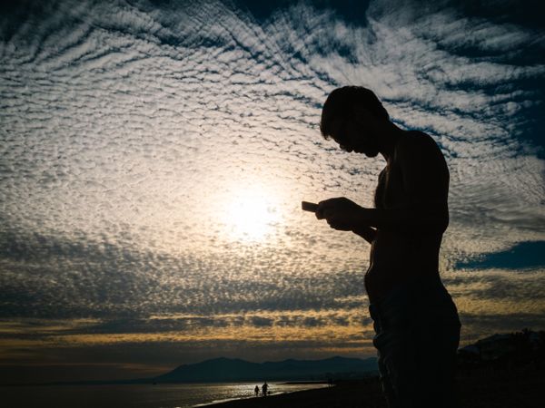 Man with smartphone against cloudy evening sky