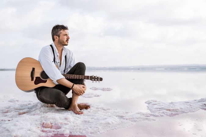Musician with guitar on pink sandy water
