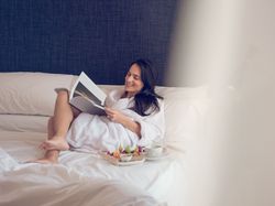 Smiling woman reading magazine during breakfast on bed