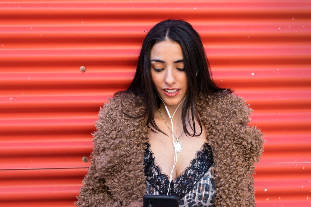 Trendy woman with smartphone near wall