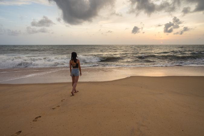 Woman in beachwear walking on sand barefoot