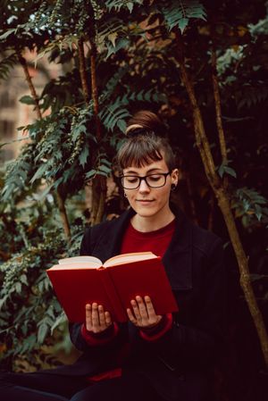 Young woman reading book on bench in park