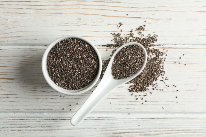 Ceramic sauce boat and spoon with chia on wooden background, top view