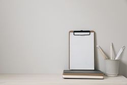 Wooden clipboard mockup with blank paper sheet on a wooden table with cup of pencils