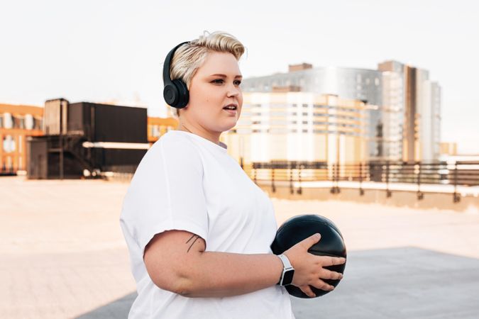 Fit blonde woman with medicine ball and headphones on a rooftop