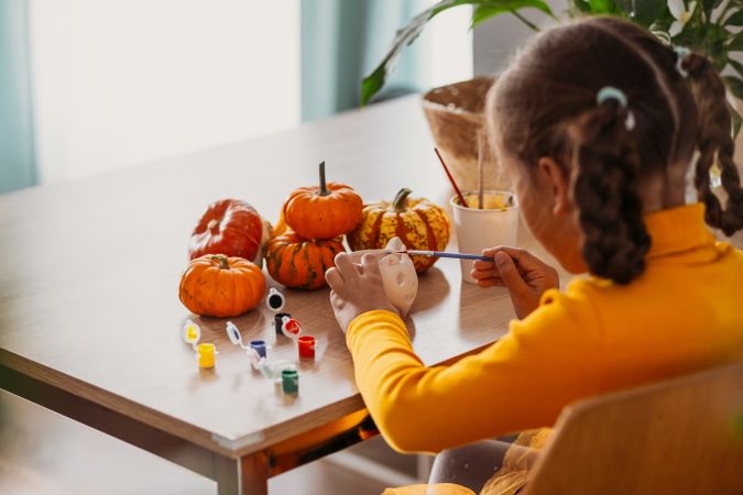 A little girl paints a clay hand made pumpkin. Halloween party. Crafts for children.