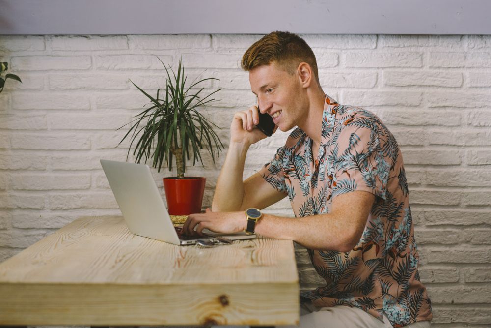 Man talking on smartphone while browsing laptop