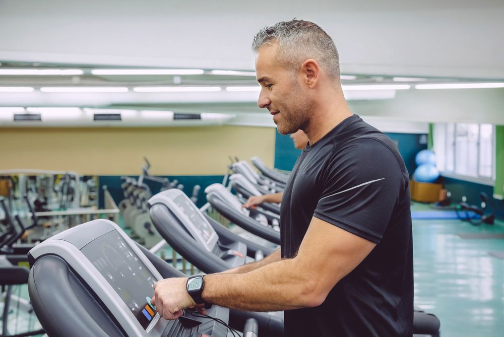 Side view of fit male adjusting screen of treadmills in gym