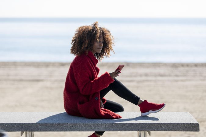 Side view of female checking smart phone on bench by the sea