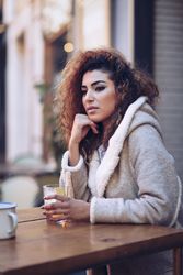 Woman sitting at wooden table of outdoor bar with drink
