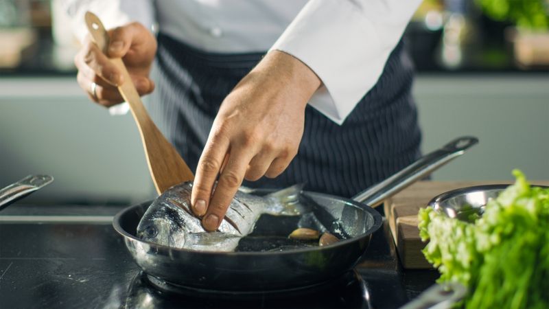 Famous Restaurant Chef Turns Over Fish on a Hot Pan. Close-up Shot of Pan with Picturesque Vegetables Seen.