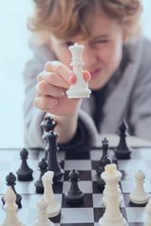 Preteen boy squinting and showing chess of piece queen