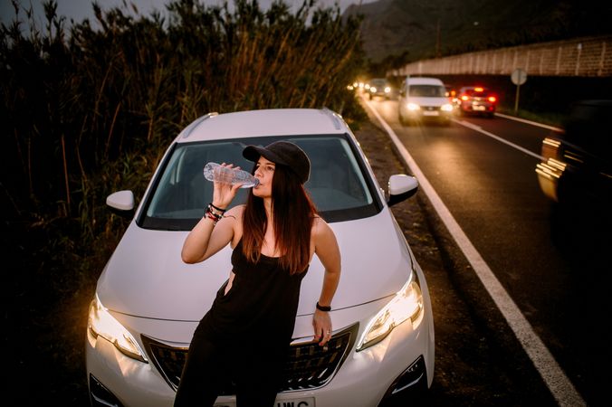 Woman drinking water near car on road at night