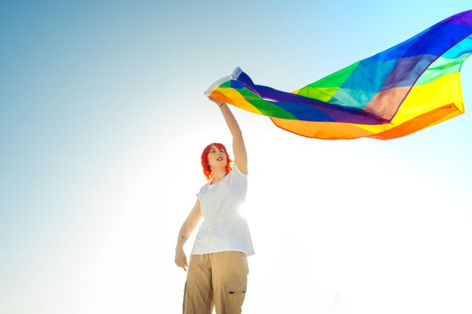 Young woman waving rainbow flag under blue sky