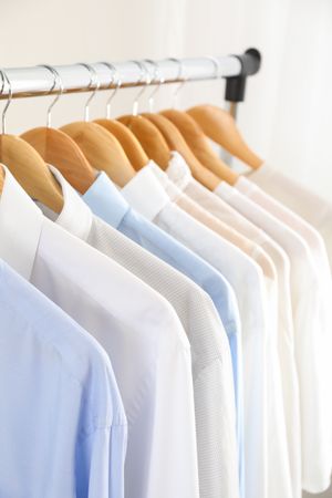 Hangers with shirts against light background, close up