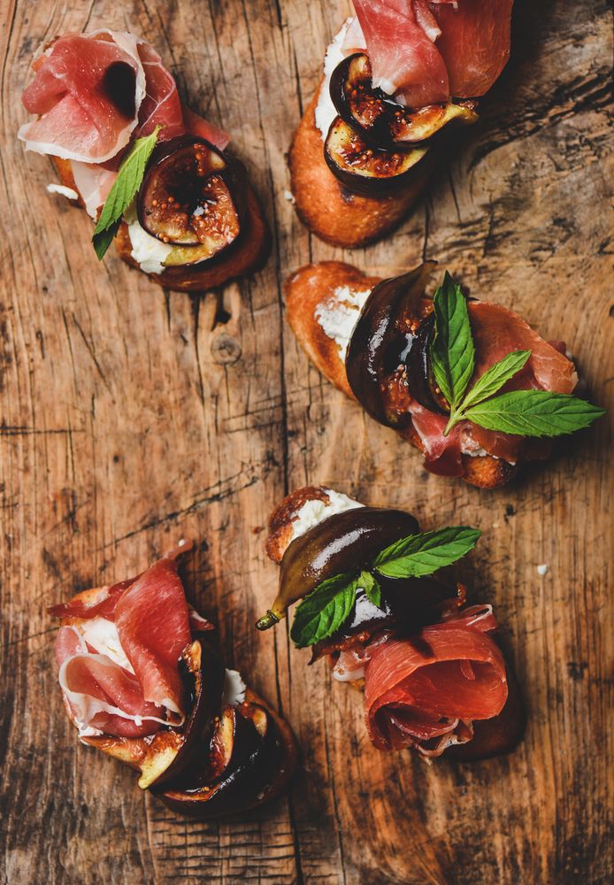 Crostinis with prosciutto, goat cheese and grilled figs on wooden board
