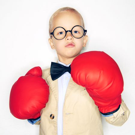 Serious blond boy wearing round glasses and red boxing gloves and suit with bow tie