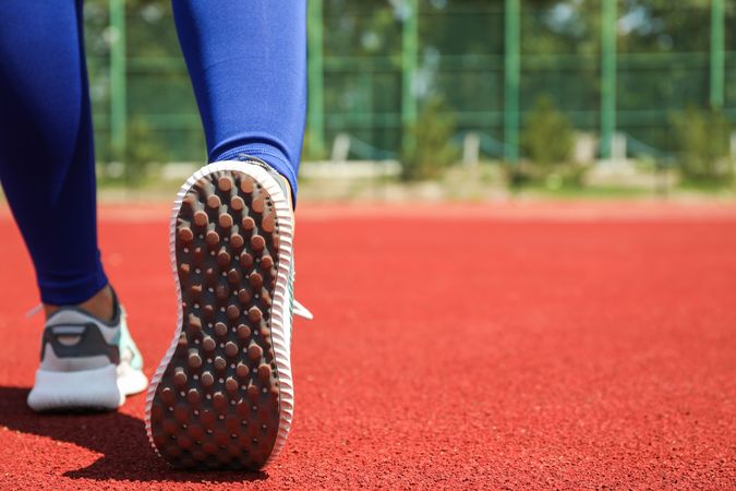 Girl walking on red athletic track, space for text