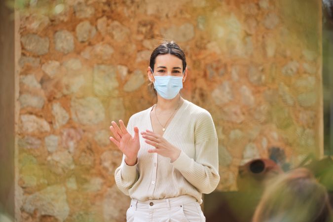 Content woman in mask standing against stone wall in garden
