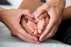 Baby feet surrounded by the hands of their heart-shaped parents