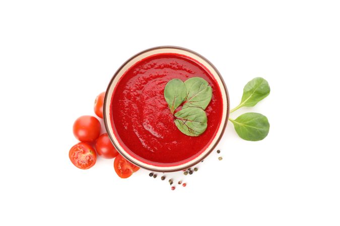 Top view of bowl of tomato soup with fresh ingredients in bright room