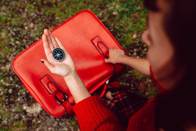 Woman with red suitcase on ground checking compass