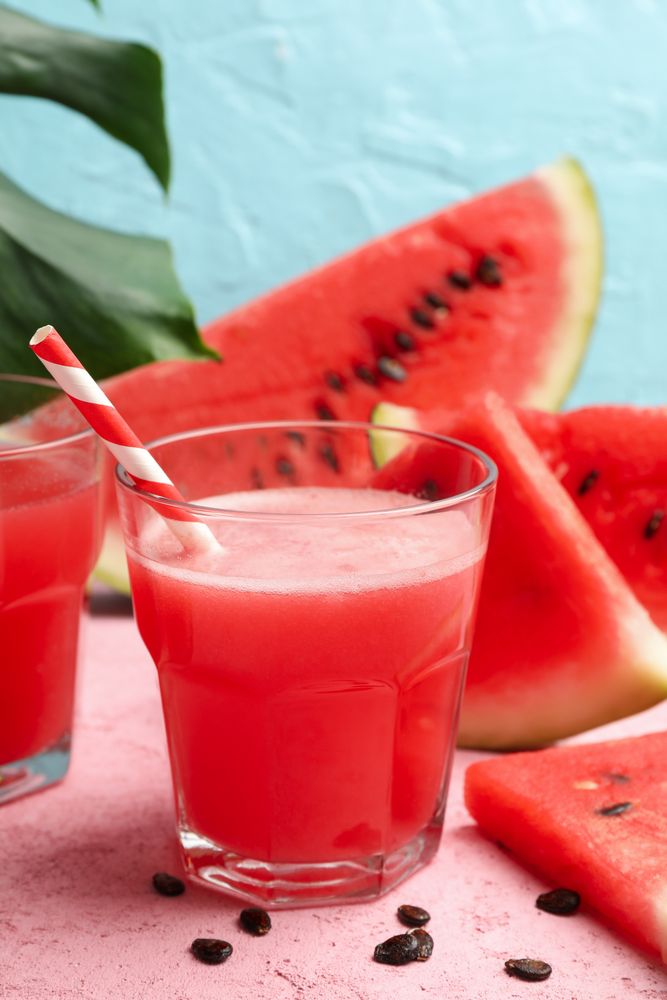 Composition with glass of watermelon juice and slices on pink table