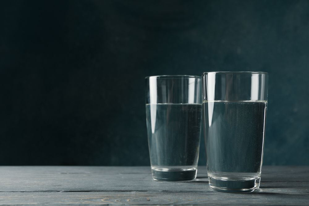 Two glasses of water in dark room on marble table, copy space