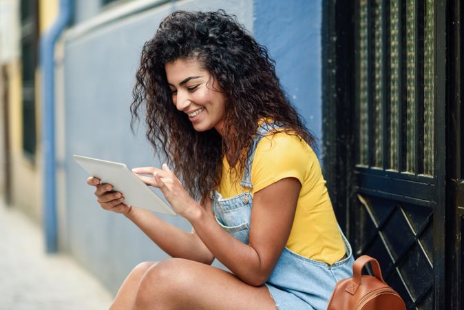 Smiling Arab woman looking at her digital tablet sitting outside a door