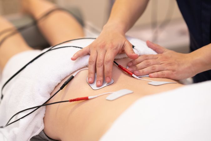 Physiotherapist placing electro pads on lower back of woman
