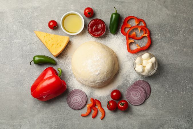 Dough and ingredients for cooking pizza on gray background