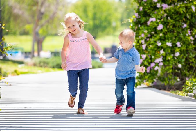 Young Sister and Brother Holding Hands And Running At The Park