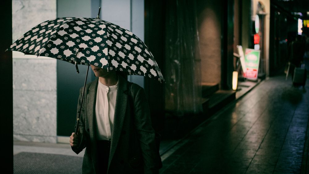 Person in green coat holding umbrella walking on sidewalk at nighttime