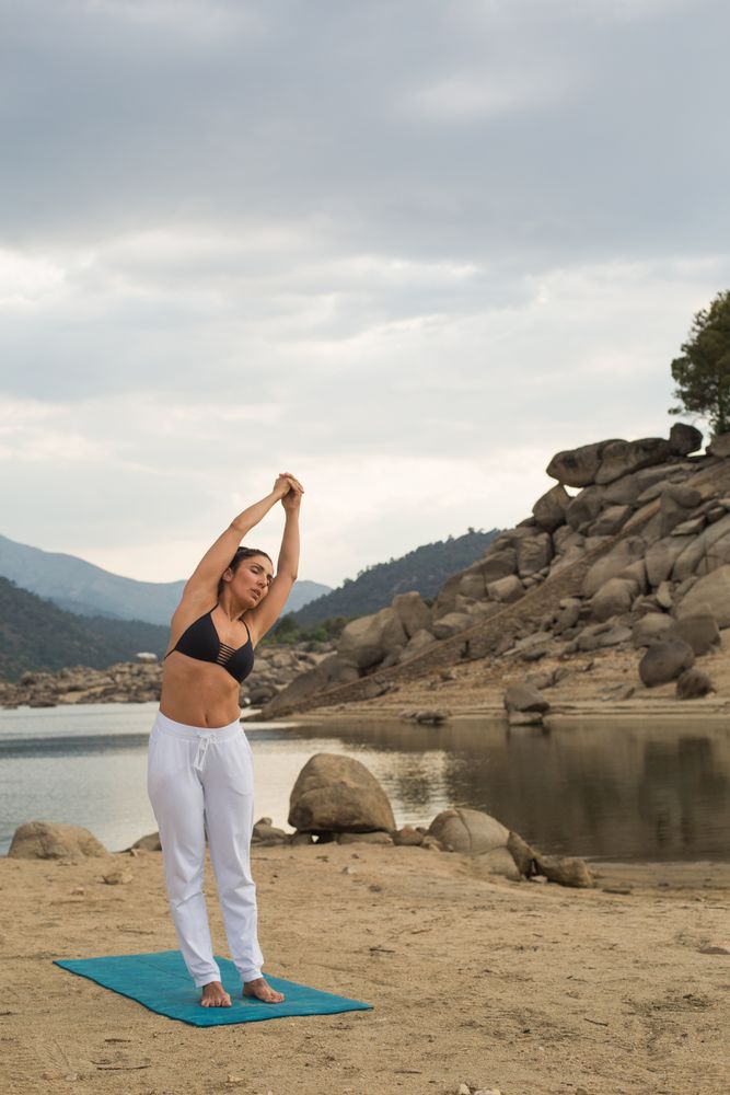 Woman practicing yoga outdoors near water