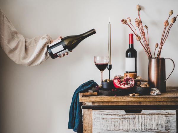 Rustic setting of woman with bottle of wine wine, cheese, long candles, pomegranate, dried poppies