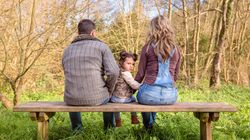 Back of parents with small girl looking around on park bench looking out to forest