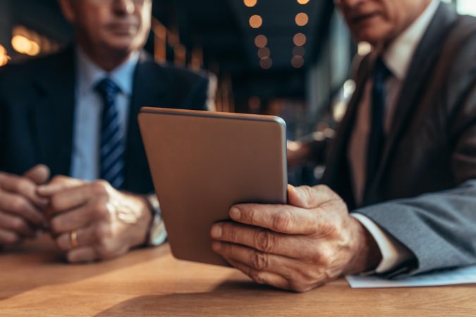 Close up of digital tablet in hand of businessman talking to his partner