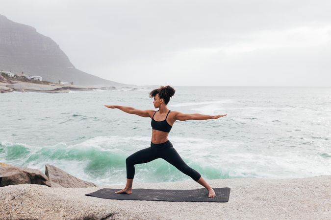 Female stretching with open arms in warrior pose while next to the ocean