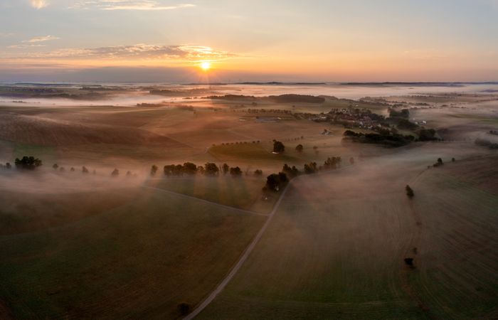 Drone image of rolling agricultural fields covered in fog at golden hour
